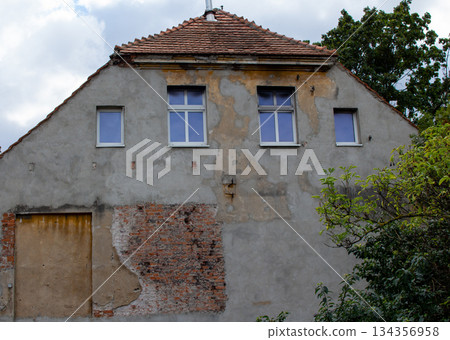 Old building with peeling paint and exposed bricks under a cloudy sky Old building with peeling paint and exposed bricks under a cloudy sky 134356958