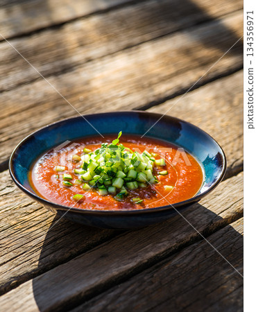 Bowl of refreshing gazpacho soup with fresh cucumber garnish on a wooden table 134356971
