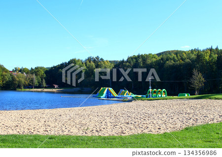 Colorful water park features and sandy beach beside a serene lake surrounded Colorful water park features and sandy beach beside a serene lake surrounded 134356986