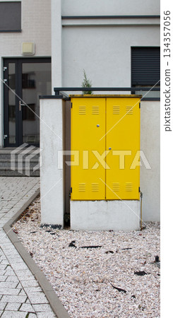 Bright yellow utility box stands out in modern urban setting with white gravel 134357056