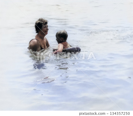 Vintage portrait of a happy mother and son playing in water on the seashore. Retro photo, 1971. Vintage portrait of a happy mother and son playing in water on the seashore. Retro photo, 1971. 134357250