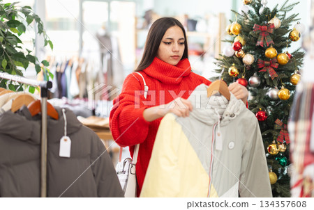 Young girl choosing down jacket in clothing store Young girl choosing down jacket in clothing store 134357608