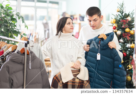 Couple standing in shop and choosing warm winter clothes in Christmas shop Couple standing in shop and choosing warm winter clothes in Christmas shop 134357634