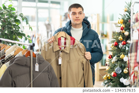 Young guy choosing raincoat in clothing store 134357635