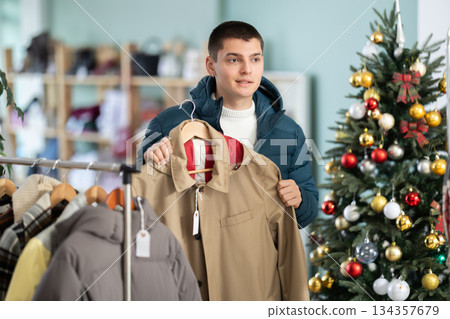 Young guy choosing raincoat in clothing store 134357679