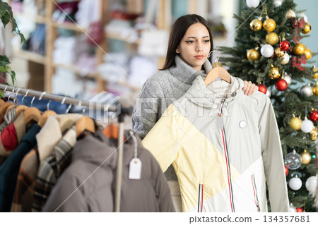 Young woman choosing coat and jacket in Christmas shop Young woman choosing coat and jacket in Christmas shop 134357681