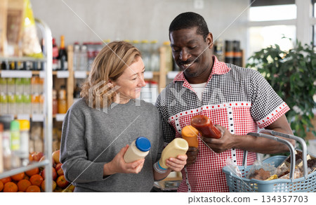 African man with European wife buyer select thoughtfully at bottles of different sauces African man with European wife buyer select thoughtfully at bottles of different sauces 134357703