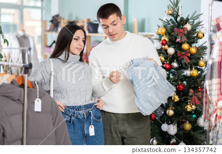 Married couple choose jeans against background of Christmas tree in clothing store 134357742