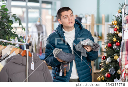 Male shopper chooses warm hat in clothing store before Christmas 134357756