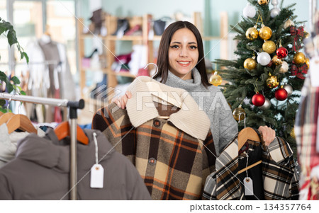 Young woman chooses coat or down jacket in clothing store Young woman chooses coat or down jacket in clothing store 134357764