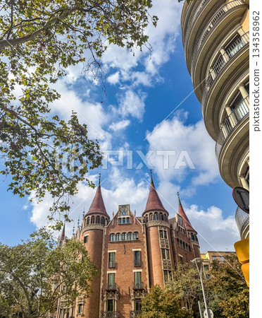 Scenic city view of a red brick historic building with pointed towers and leafy trees under a blue sky. Travel, architecture, and European heritage concept. High quality photo 134358962