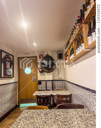 Warm cozy restaurant interior with wine bottles on shelves, tiled walls, and wooden furniture. Authentic Spanish dining atmosphere and travel concept. High quality photo 134358972