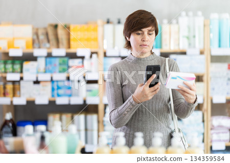 Woman in autumn clothes scans code on package of pills to check expiration date Woman in autumn clothes scans code on package of pills to check expiration date 134359584