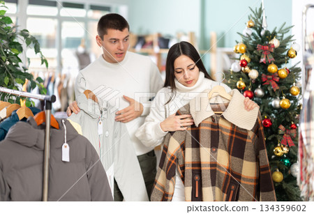 Portrait of happy married couple choose coat or jacket for girl against background of Christmas tree in store Portrait of happy married couple choose coat or jacket for girl against background of Christmas tree in store 134359602