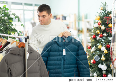 Male shopper choose down jacket in clothing store before Christmas 134359666