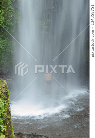 Vertical view of a person standing behind the curtain of a powerful, long exposure waterfall in Bayan, North Lombok, Indonesia. Vertical view of a person standing behind the curtain of a powerful, long exposure waterfall in Bayan, North Lombok, Indonesia. 134359751