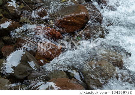Close up fresh waterfall stream rushing over wet brown river rocks texture in a natural setting. 134359758