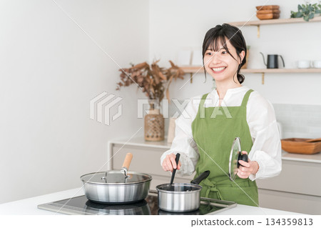 Young Asian woman in an apron cooking in the kitchen Young Asian woman in an apron cooking in the kitchen 134359813