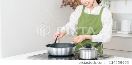 年輕的亞裔女子穿著圍裙在廚房做飯 年輕的亞裔女子穿著圍裙在廚房做飯 134359993