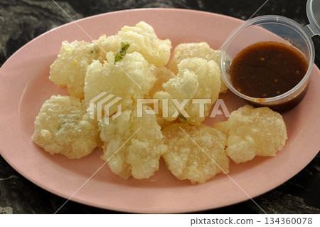 Crispy Cireng, traditional Indonesian street food made from fried tapioca starch, served close-up on a pink plastic plate with spicy brown dipping sauce. Crispy Cireng, traditional Indonesian street food made from fried tapioca starch, served close-up on a pink plastic plate with spicy brown dipping sauce. 134360078