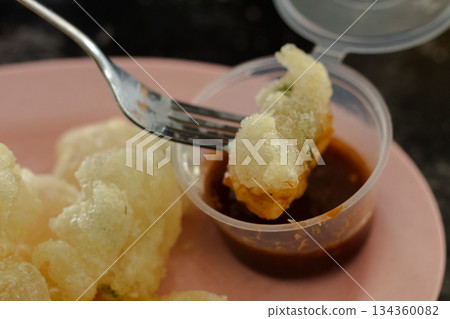 Macro shot of Indonesian Cireng (fried tapioca starch snack) being dipped by a fork into traditional sweet chili dipping sauce. Macro shot of Indonesian Cireng (fried tapioca starch snack) being dipped by a fork into traditional sweet chili dipping sauce. 134360082