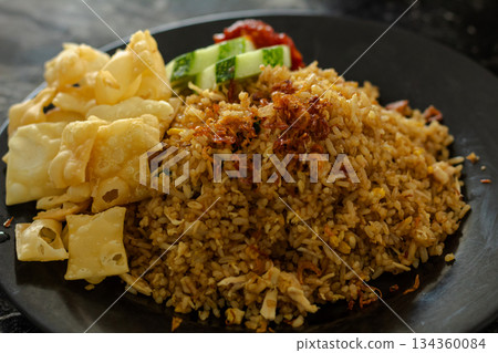Authentic Indonesian Nasi Goreng served hot, garnished with fried shallots, shredded chicken, alongside crispy pangsit crackers, fresh cucumber, and spicy chili paste. Authentic Indonesian Nasi Goreng served hot, garnished with fried shallots, shredded chicken, alongside crispy pangsit crackers, fresh cucumber, and spicy chili paste. 134360084