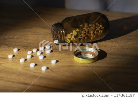 White pills spilled on a table and a brown opaque bottle White pills spilled on a table and a brown opaque bottle 134361197