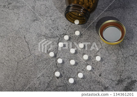 White pills spilled on a table and a brown opaque bottle 134361201