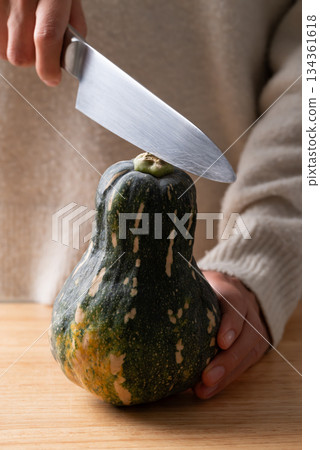 Hand holding kitchen knife and cutting green butternut squash on wooden board 134361618