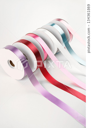 Colorful plastic ribbon rolls arranged in a row on a white background, with each strip pulled forward, ideal for floral wrapping, crafts, and gift decoration. 134361869