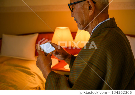 一位老年男子在臥室操作智慧型手機 一位老年男子在臥室操作智慧型手機 134362366