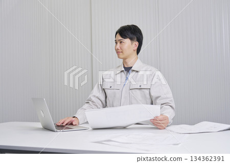 A man working at a construction company sitting with a blueprint, indoor portrait A man working at a construction company sitting with a blueprint, indoor portrait 134362391