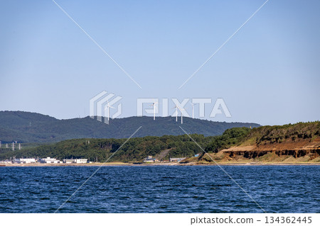 Wind turbines lined up on a clear blue sea and green hills Wind turbines lined up on a clear blue sea and green hills 134362445