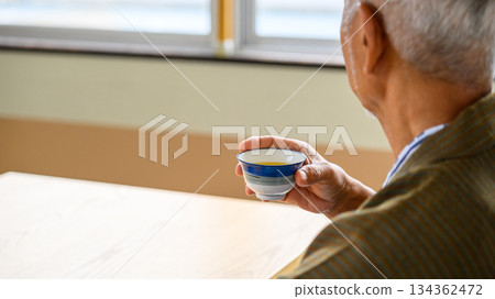 Rear view of an elderly man drinking tea from a teacup 134362472