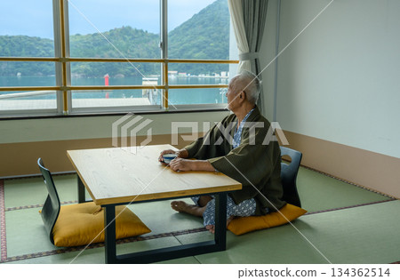 一位老人在客棧裡一邊喝茶一邊欣賞風景。 一位老人在客棧裡一邊喝茶一邊欣賞風景。 134362514