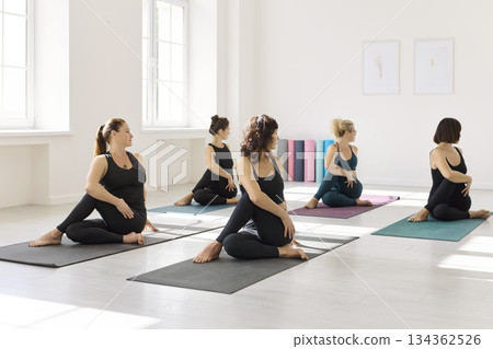 Women practicing seated spinal twist in a bright yoga studio during group class 134362526