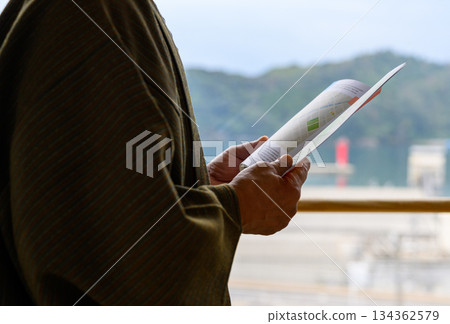 An elderly man in a kimono reading a pamphlet 134362579