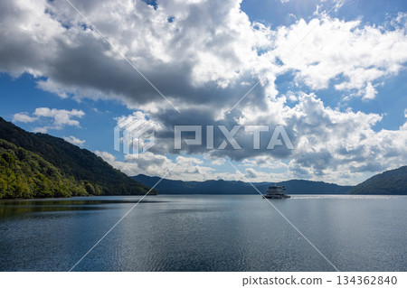 Lake Towada surrounded by green mountains and a white sightseeing boat sailing on the lake 134362840