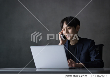 一位年輕的商人一邊看著電腦，一邊用智慧型手機聊天 134362865