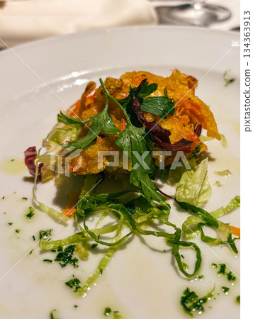 Gourmet appetizer of crispy fried bites with fresh salad greens and herbs, elegantly drizzled with olive oil on a white plate, refined presentation for fine dining 134363913