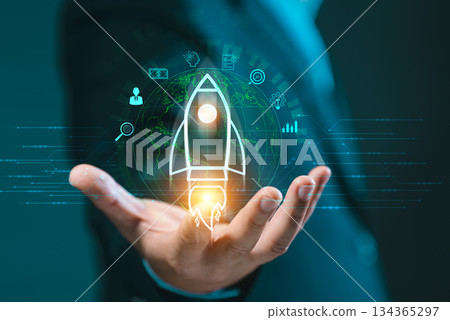 Hand presenting a glowing rocket icon over a global network, surrounded by business symbols. Signifies startup launch, innovation, future vision, and business acceleration. 134365297