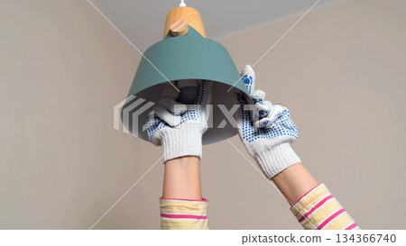 Close-up of a woman carefully installing a new light bulb wearing protective gloves and working in a well-lit inviting home environment Close-up of a woman carefully installing a new light bulb wearing protective gloves and working in a well-lit inviting home environment 134366740