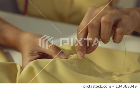 Asian woman threading the needle. Tailor working in her studio with focus in hands putting thread in sewing needle. Asian woman threading the needle. Tailor working in her studio with focus in hands putting thread in sewing needle. 134368349