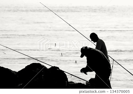 Silhouettes of Bosphorus fishermen in the early morning. A black-and-white, high-contrast image that captures the serene solitude of recreational fishing in Istanbul. 134370005