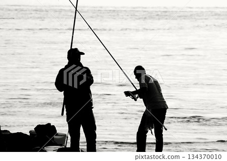 Silhouettes of Bosphorus fishermen in the early morning. A black-and-white, high-contrast image that captures the serene solitude of recreational fishing in Istanbul. Silhouettes of Bosphorus fishermen in the early morning. A black-and-white, high-contrast image that captures the serene solitude of recreational fishing in Istanbul. 134370010