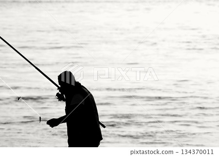 Silhouettes of Bosphorus fishermen in the early morning. A black-and-white, high-contrast image that captures the serene solitude of recreational fishing in Istanbul. Silhouettes of Bosphorus fishermen in the early morning. A black-and-white, high-contrast image that captures the serene solitude of recreational fishing in Istanbul. 134370011