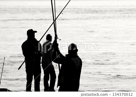 Silhouettes of Bosphorus fishermen in the early morning. A black-and-white, high-contrast image that captures the serene solitude of recreational fishing in Istanbul. Silhouettes of Bosphorus fishermen in the early morning. A black-and-white, high-contrast image that captures the serene solitude of recreational fishing in Istanbul. 134370012