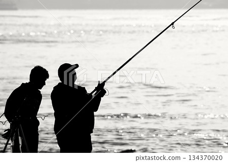Silhouettes of Bosphorus fishermen in the early morning. A black-and-white, high-contrast image that captures the serene solitude of recreational fishing in Istanbul. 134370020