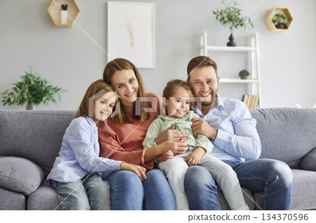 Portrait of cheerful smiling young happy family of four with two kids sitting on sofa at home Portrait of cheerful smiling young happy family of four with two kids sitting on sofa at home 134370596