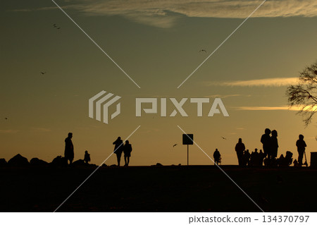 Silhouettes Walking by the Sea at Sunset. Silhouettes Walking by the Sea at Sunset. 134370797
